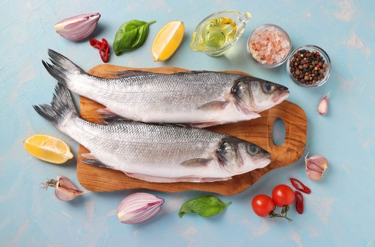 Dos lubinas frescas con ingredientes en fondo celeste Dos lubinas frescas con ingredientes en fondo celeste