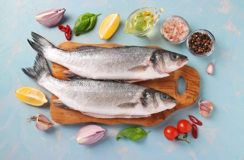 Dos lubinas frescas con ingredientes en fondo celeste