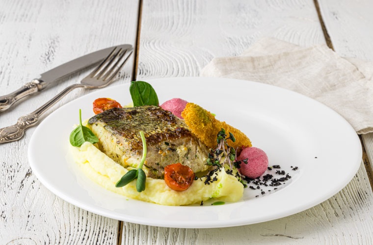 Plato de pescado en mesa con cubiertos Plato de pescado en mesa con cubiertos
